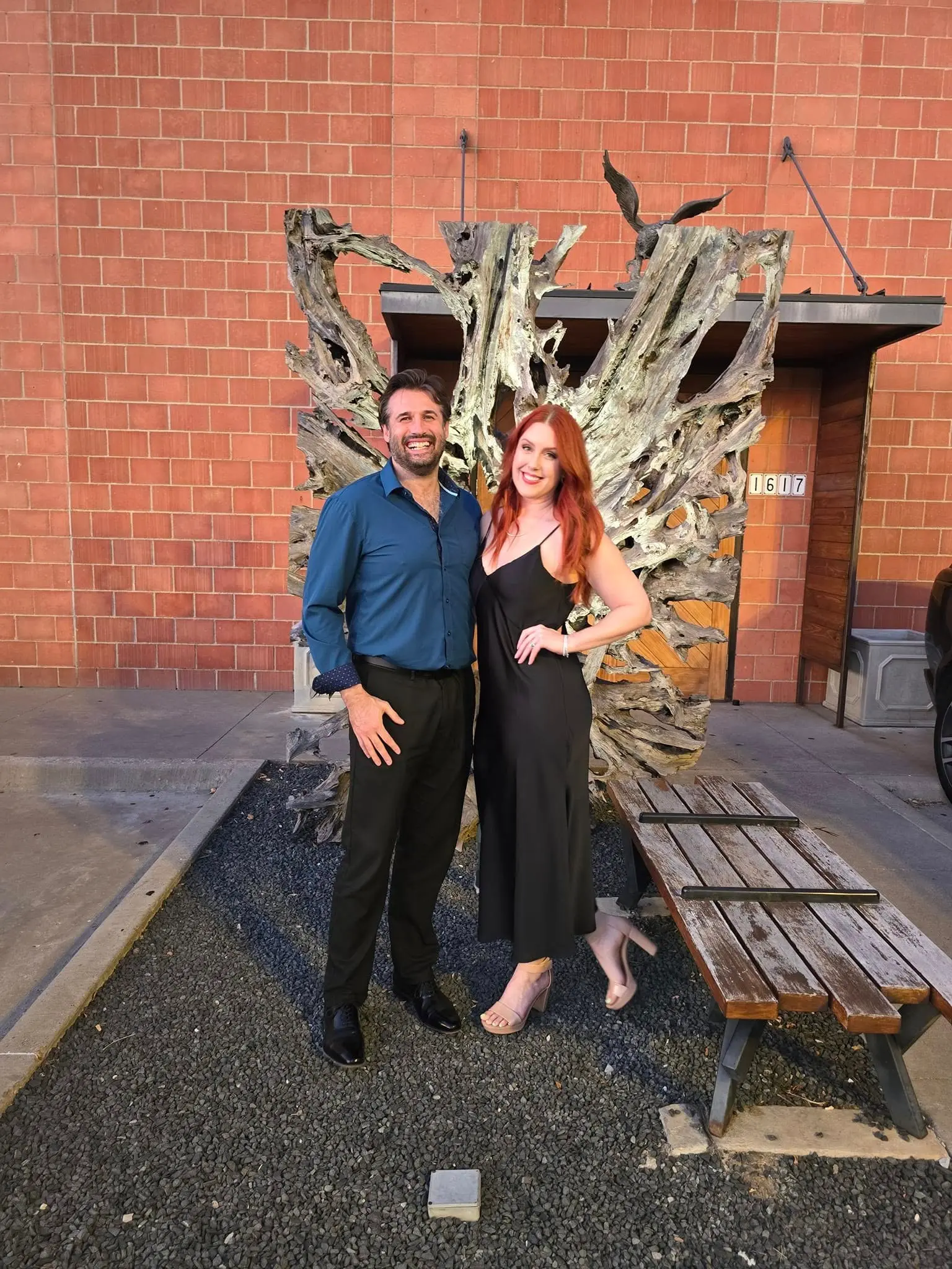 Mitch and Brittany dressed up in front of a driftwood sculpture on a brick building