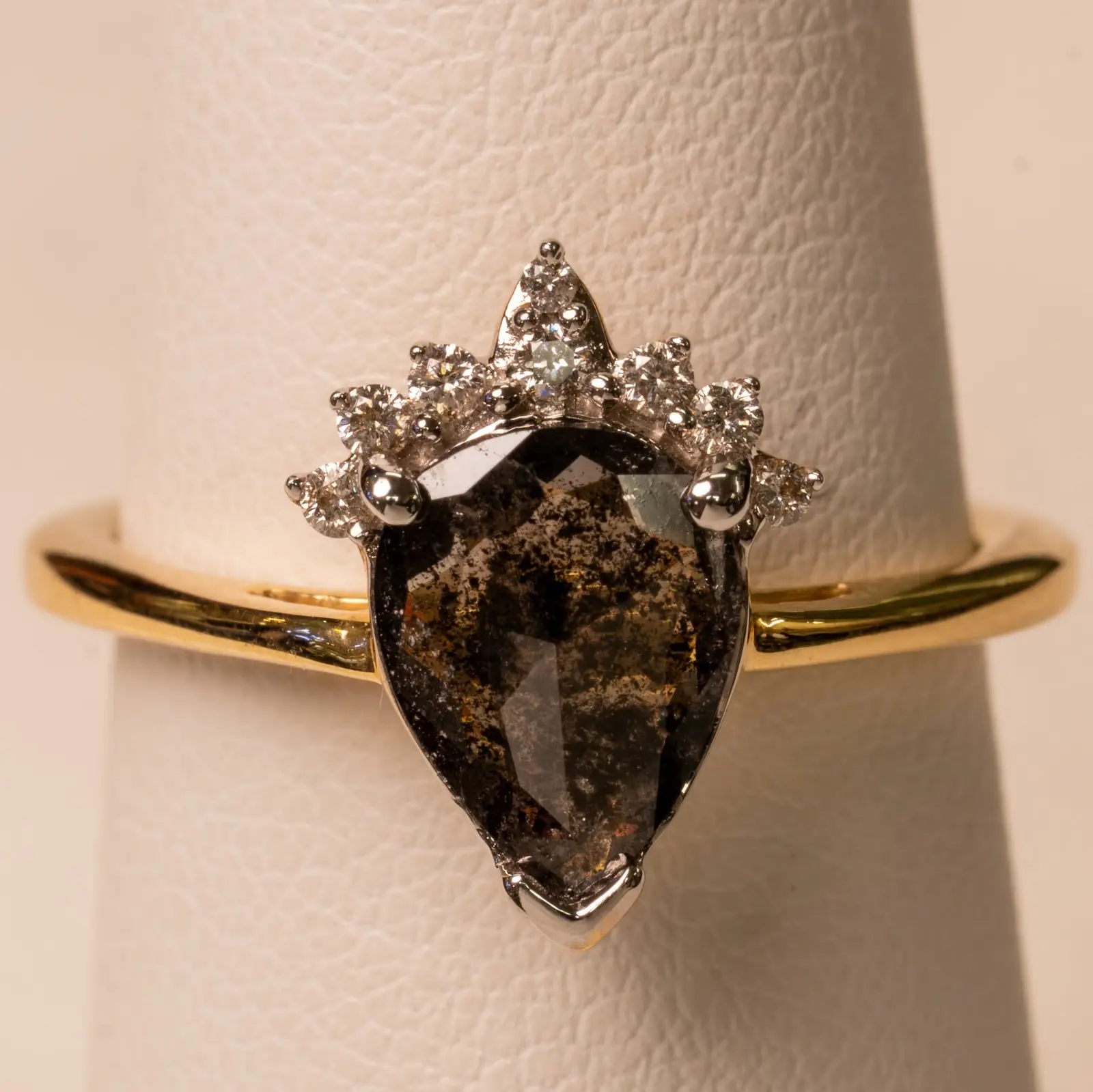 Salt and pepper pear diamond ring with a crown-style halo, on a ring holder