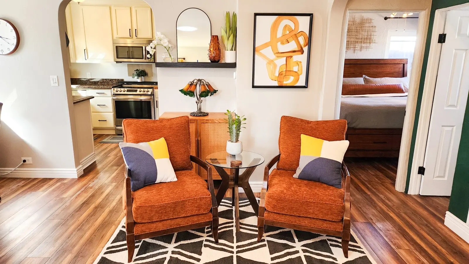 Sitting area at The Elati House with two orange armchairs, a geometric rug and an open kitchen behind