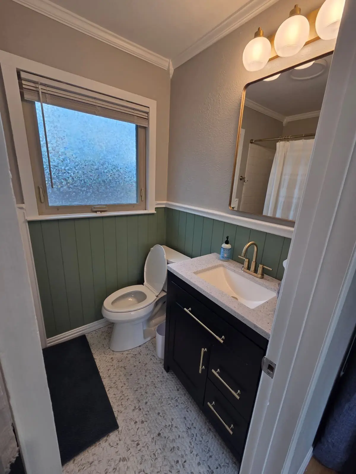 The McCosh Apartment bathroom with a black vanity and green wainscoting
