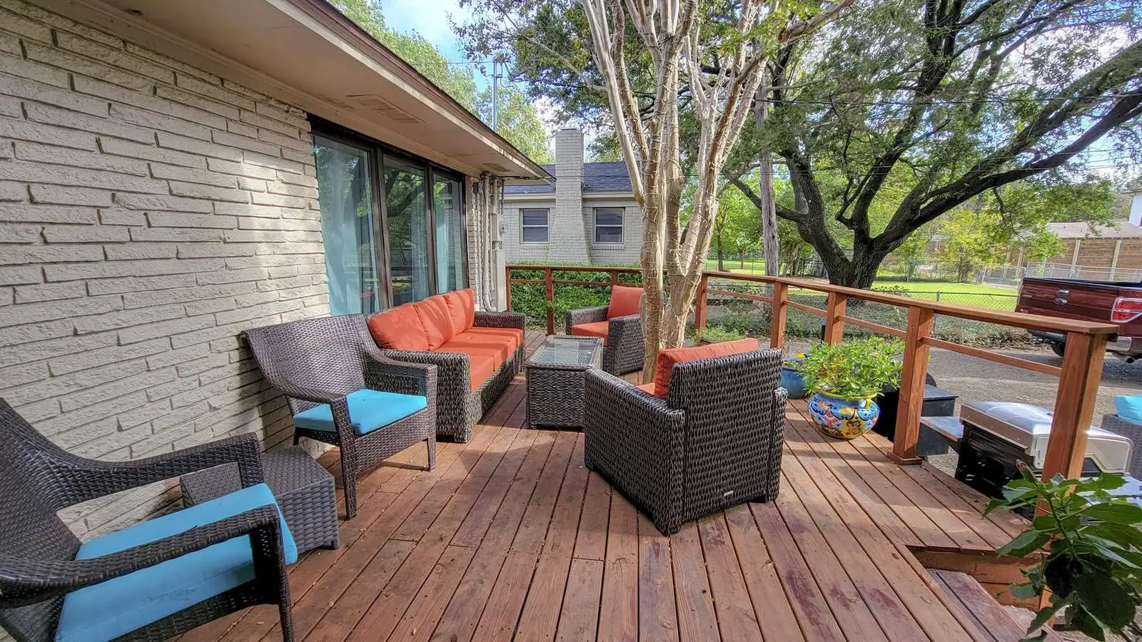 Wood deck at The McCosh House with wicker chairs, orange and turquoise cushions, and trees beyond